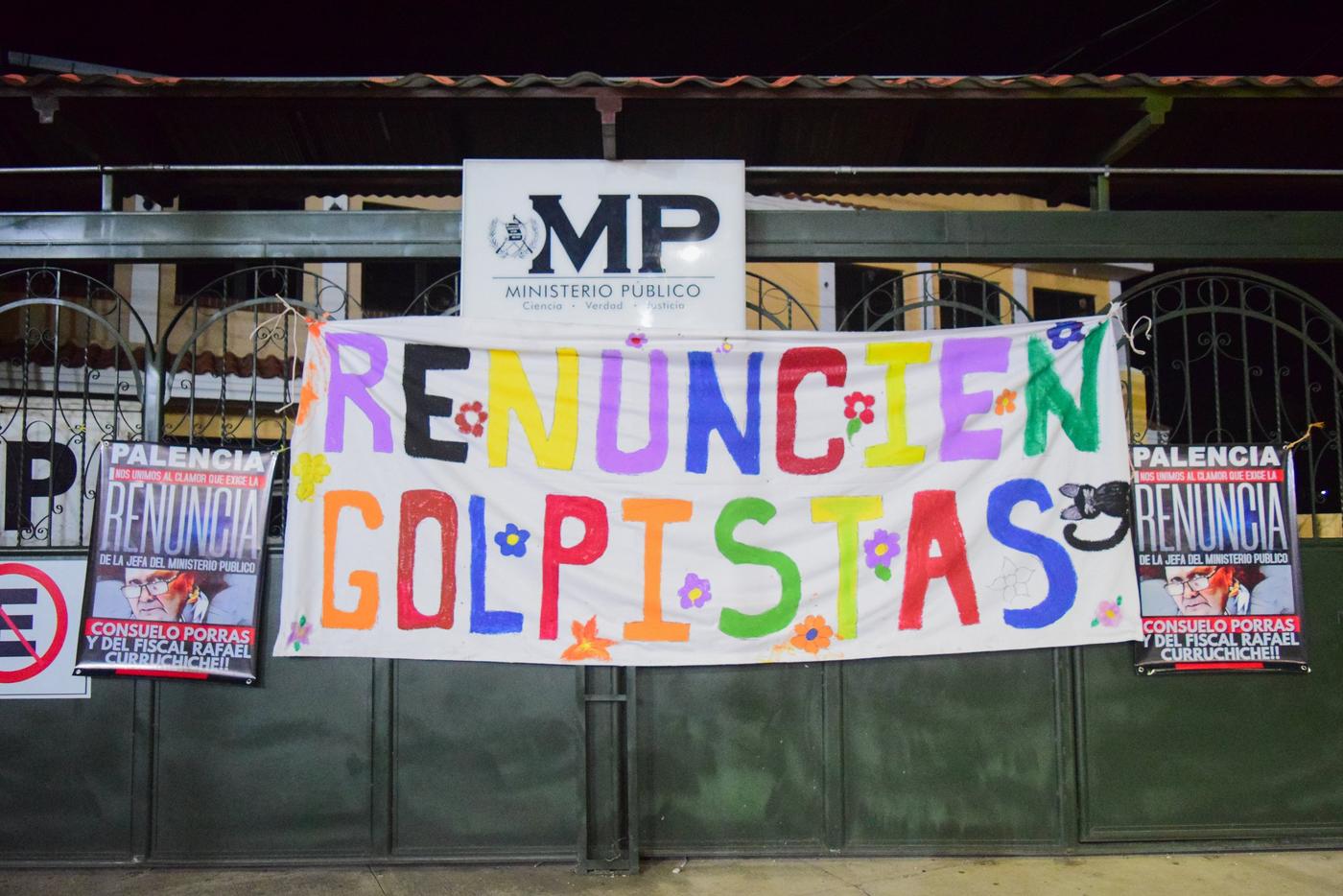  “Renuncien golpistas”, voces de resistencia y unidad del pueblo palenciano. El mensaje aparece en una manta pintada a mano por la población, floreciendo con colores y mensajes de esperanza, frente al Ministerio Público durante el paro nacional. Municipio de Palencia, Guatemala, 7 de octubre de 2023. Foto de Maylin Hernández 